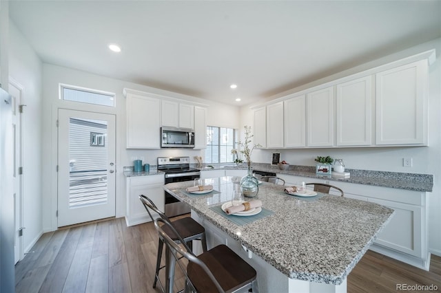 kitchen featuring appliances with stainless steel finishes, white cabinets, light stone counters, a breakfast bar, and a center island