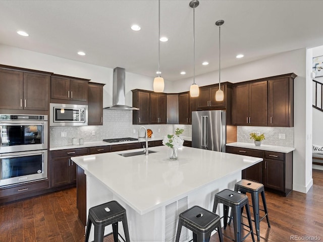 10235 E 59th Ave, Denver, CO 80238 - kitchen featuring stainless steel appliances, wall chimney range hood, a kitchen bar, dark brown cabinetry, and recessed lighting