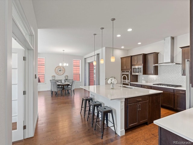 10235 E 59th Ave, Denver, CO 80238 - kitchen with wall chimney exhaust hood, stainless steel appliances, an island with sink, light countertops, and a breakfast bar