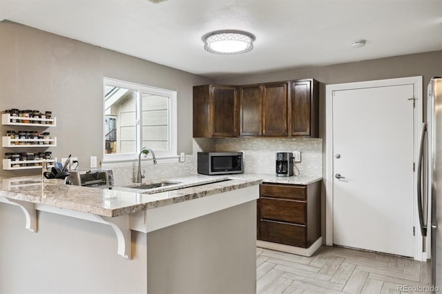 21125 E 43rd Ave, Denver, CO 80249 - kitchen featuring appliances with stainless steel finishes, a sink, backsplash, dark brown cabinets, and a kitchen bar