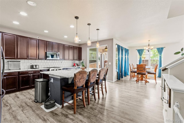 7018 E 123rd Pl, Thornton, CO 80602 - kitchen featuring stainless steel microwave, light wood-type flooring, a kitchen island with sink, backsplash, and recessed lighting