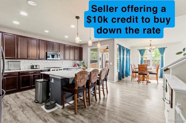 7018 E 123rd Pl, Thornton, CO 80602 - kitchen featuring stainless steel microwave, light wood-style floors, decorative backsplash, a center island with sink, and recessed lighting