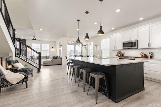 kitchen featuring a sink, light wood-style flooring, stainless steel microwave, a kitchen island with sink, and decorative backsplash