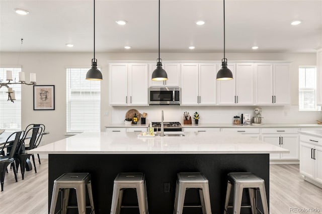 kitchen featuring stainless steel microwave, a kitchen bar, white cabinetry, and decorative backsplash