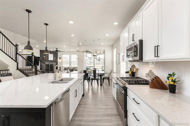 kitchen with stainless steel appliances, decorative backsplash, a sink, ceiling fan, and a kitchen island with sink