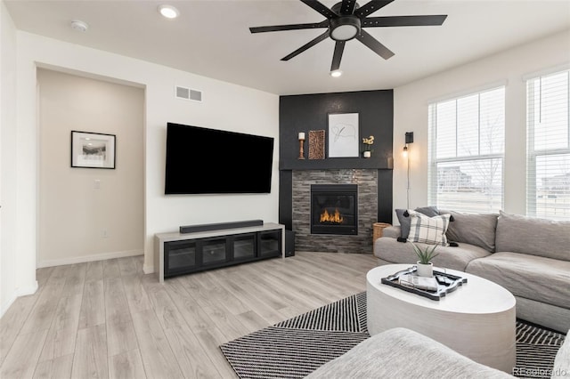 living area with visible vents, baseboards, wood finished floors, a ceiling fan, and a glass covered fireplace