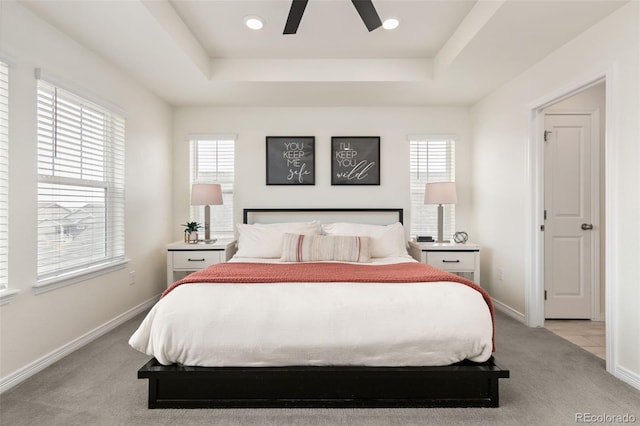 bedroom featuring light carpet, multiple windows, baseboards, and a raised ceiling