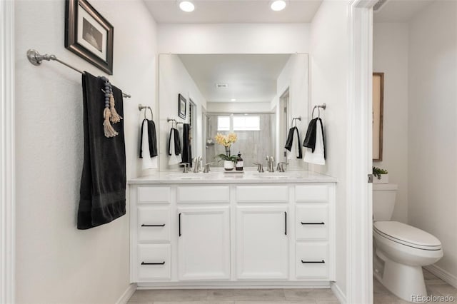full bathroom with baseboards, double vanity, a sink, and toilet