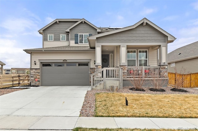 craftsman-style home featuring stone siding, fence, a garage, concrete driveway, and a porch