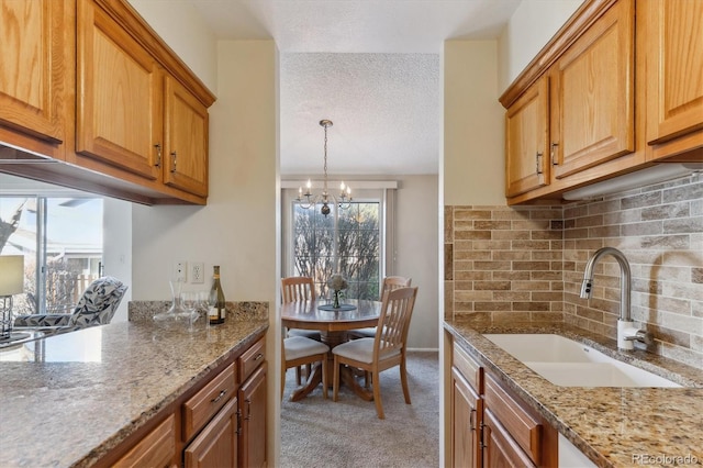 kitchen featuring light stone counters, sink, light carpet, and a textured ceiling