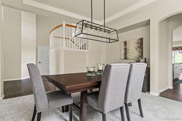 carpeted dining room featuring baseboards, arched walkways, and stairway