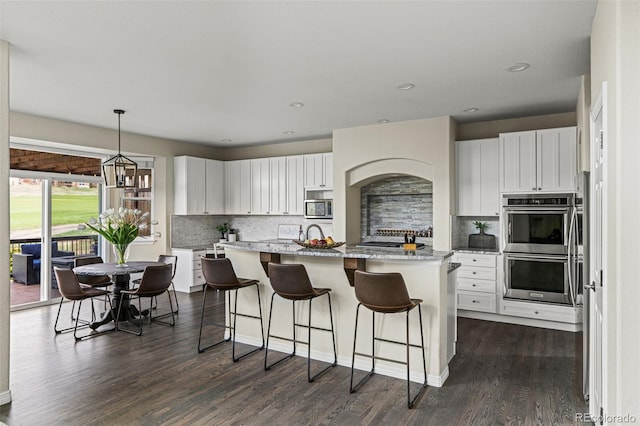 kitchen featuring a kitchen breakfast bar, dark wood-style flooring, appliances with stainless steel finishes, tasteful backsplash, and white cabinetry