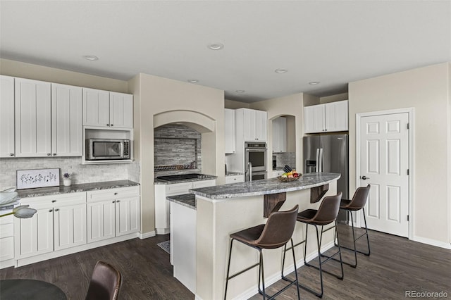 kitchen featuring a kitchen island, a kitchen breakfast bar, dark stone counters, arched walkways, and stainless steel appliances