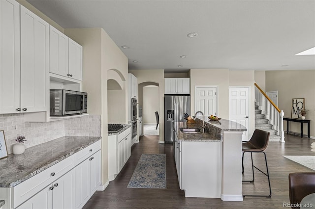 kitchen featuring stone countertops, white cabinetry, tasteful backsplash, a sink, and appliances with stainless steel finishes