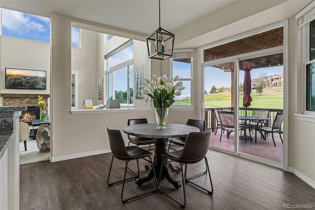 dining space with baseboards, a chandelier, a stone fireplace, and dark wood-style floors