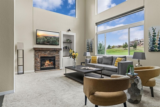 living room with a high ceiling, a stone fireplace, baseboards, and carpet