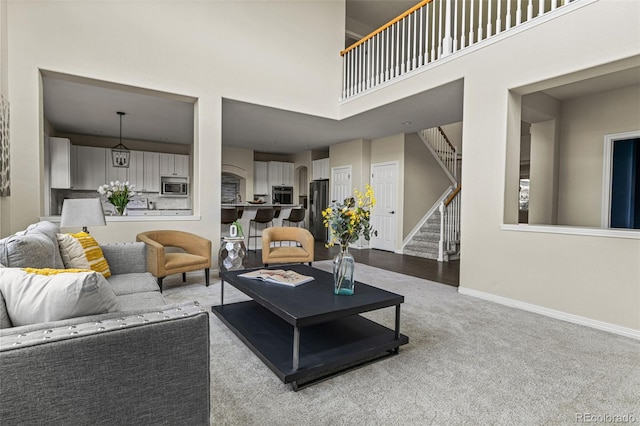 carpeted living area with a high ceiling, baseboards, and stairway