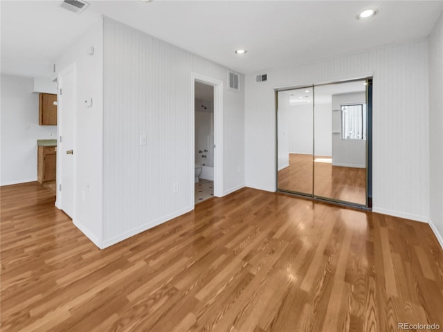 unfurnished bedroom featuring ensuite bathroom, a closet, and light wood-type flooring