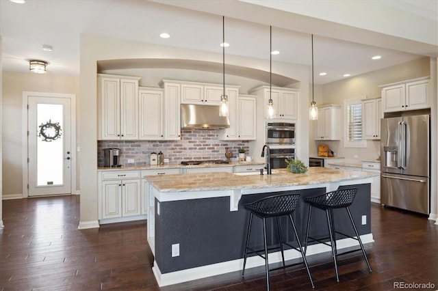 1950 W 67th Ave, Denver, CO 80221 - kitchen with a kitchen bar, under cabinet range hood, dark wood finished floors, and stainless steel appliances