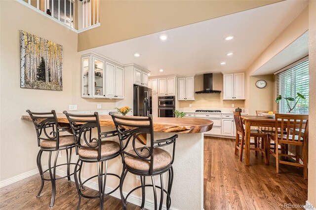 11522 Pine Grove Ln, Parker, CO 80138 - kitchen with wall chimney range hood, appliances with stainless steel finishes, a peninsula, a breakfast bar, and glass insert cabinets