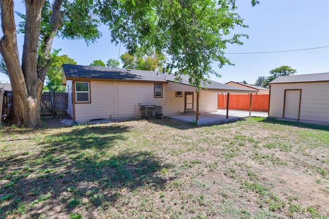 rear view of house with an outbuilding, a lawn, fence, central AC unit, and a patio area