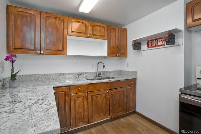 kitchen with light stone countertops, light wood-style flooring, brown cabinets, electric stove, and a sink