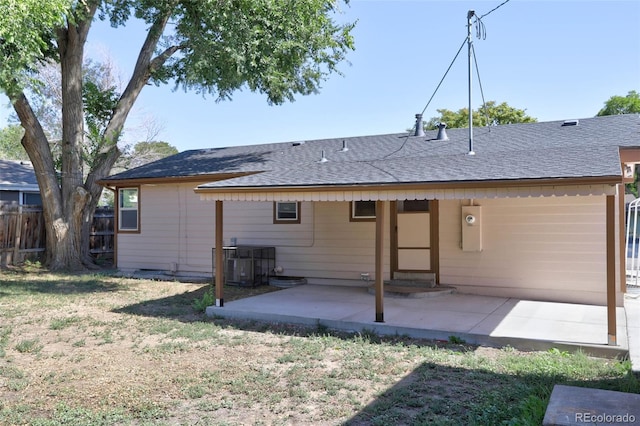 back of property with central air condition unit, a patio, fence, a yard, and a shingled roof