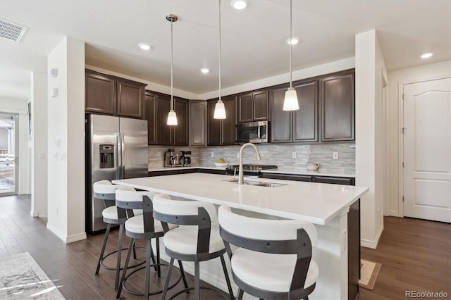 kitchen with hanging light fixtures, appliances with stainless steel finishes, a kitchen island with sink, and sink