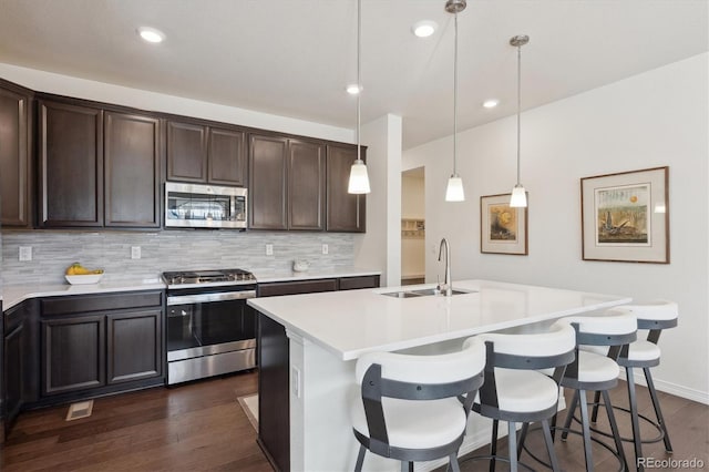 kitchen featuring sink, decorative light fixtures, stainless steel appliances, a kitchen island with sink, and backsplash