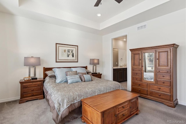 carpeted bedroom featuring connected bathroom, a tray ceiling, and ceiling fan