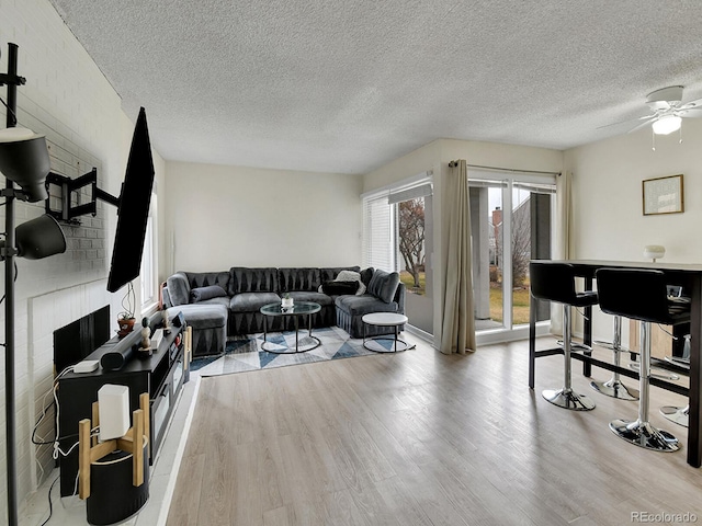 living area with a textured ceiling, a brick fireplace, ceiling fan, and light wood finished floors