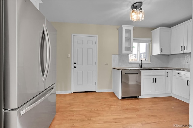 kitchen with appliances with stainless steel finishes, decorative backsplash, light wood-type flooring, and dark countertops
