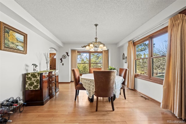 dining area with visible vents, arched walkways, a textured ceiling, light wood-type flooring, and a notable chandelier