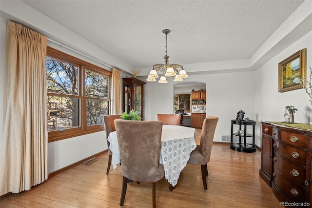 dining space featuring light wood-style floors, baseboards, a chandelier, and a textured ceiling