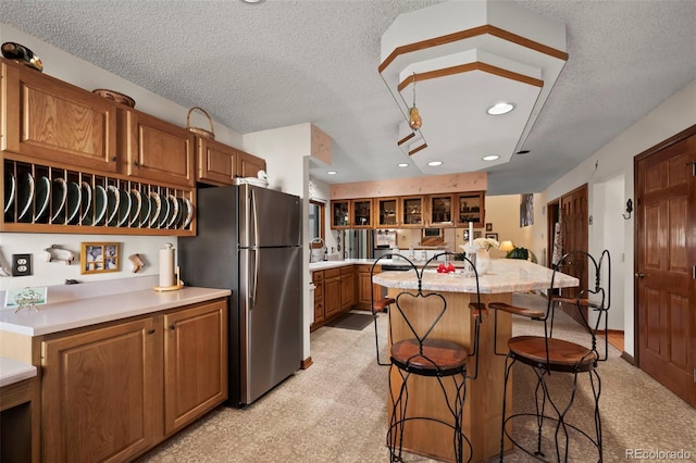 kitchen featuring brown cabinetry, a kitchen breakfast bar, a center island, freestanding refrigerator, and a textured ceiling