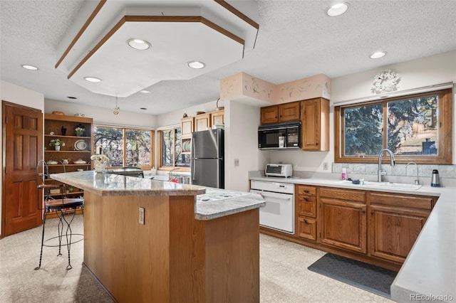 kitchen featuring a center island, freestanding refrigerator, a sink, black microwave, and oven