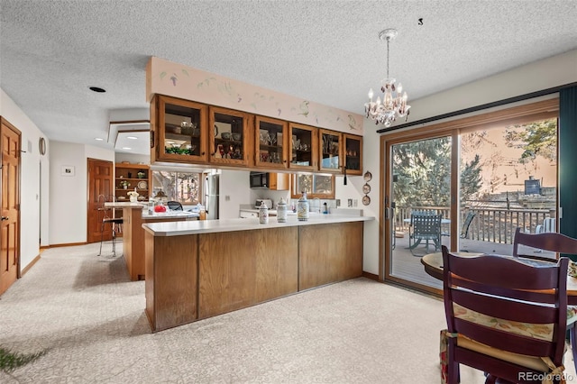 kitchen featuring light colored carpet, glass insert cabinets, brown cabinets, a peninsula, and light countertops