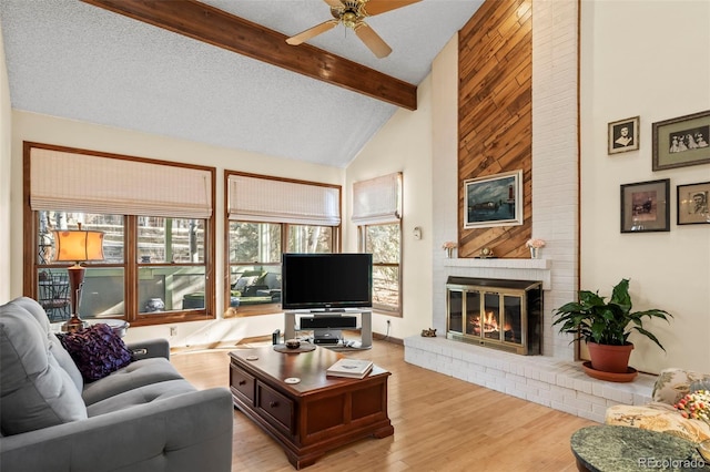 living area with light wood-type flooring, a brick fireplace, a healthy amount of sunlight, and beam ceiling