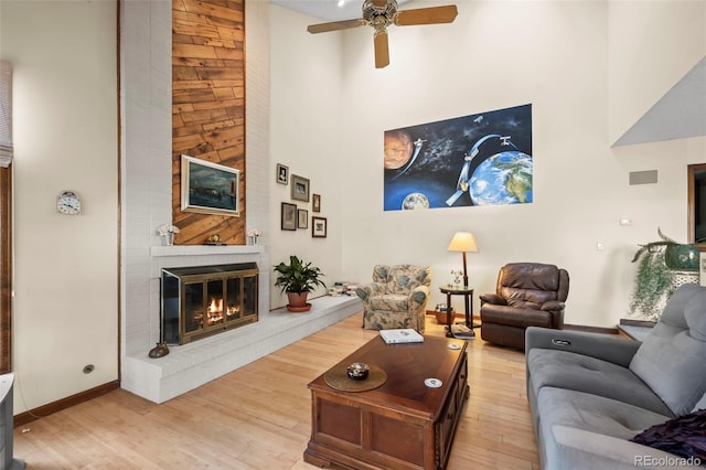 living area featuring light wood-style floors, a brick fireplace, a high ceiling, and a ceiling fan