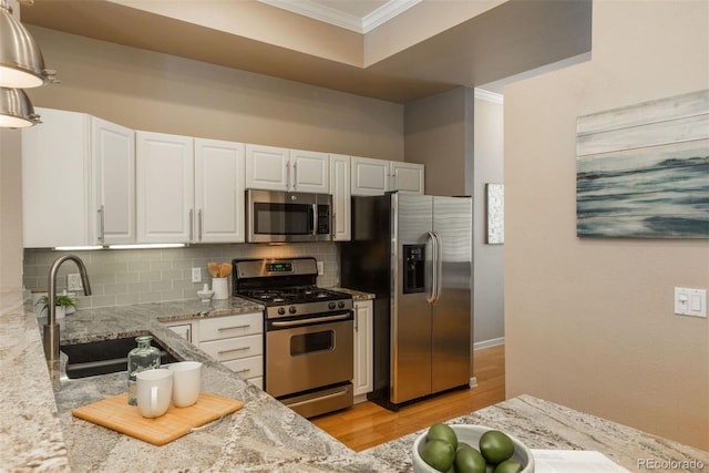 880 E 16th Ave Unit D, Denver, CO 80218 - kitchen with appliances with stainless steel finishes, ornamental molding, white cabinetry, light wood-style flooring, and decorative backsplash