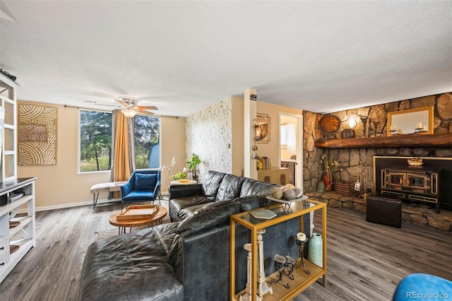 living room with a textured ceiling, wood-type flooring, ceiling fan, and a stone fireplace