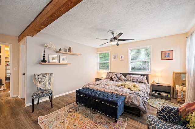 bedroom with a textured ceiling, dark wood-type flooring, ceiling fan, and beamed ceiling