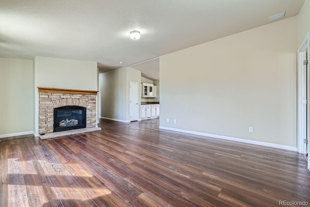 unfurnished living room featuring a textured ceiling, dark hardwood / wood-style flooring, and a stone fireplace