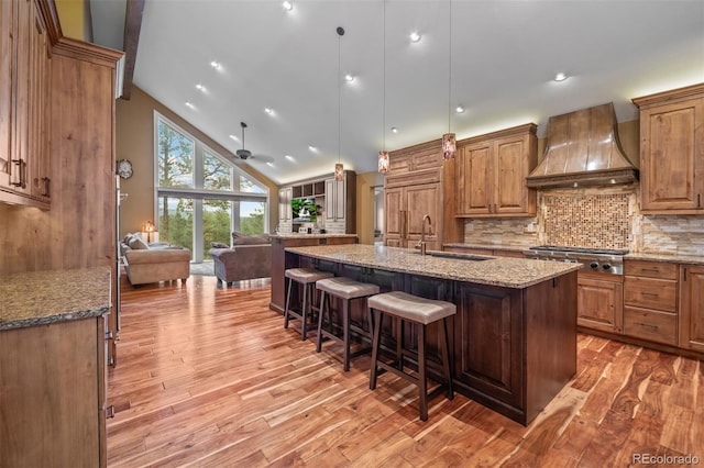 29210 Northstar Ln, Evergreen, CO 80439 - kitchen featuring premium range hood, stainless steel gas cooktop, light wood-style floors, open floor plan, and a kitchen breakfast bar