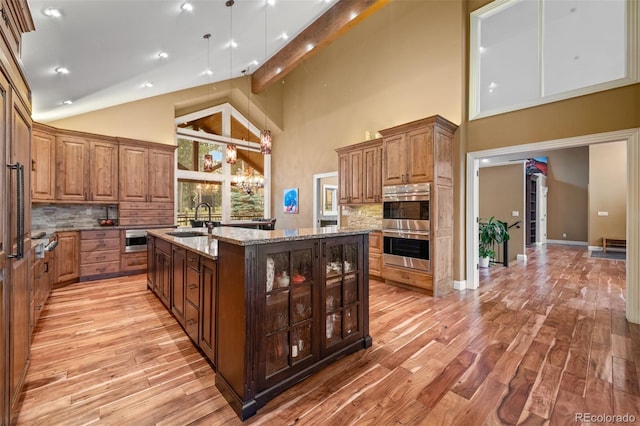 29210 Northstar Ln, Evergreen, CO 80439 - kitchen featuring an island with sink, light wood finished floors, tasteful backsplash, high vaulted ceiling, and light stone countertops