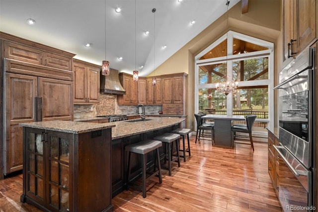 29210 Northstar Ln, Evergreen, CO 80439 - kitchen with custom range hood, an island with sink, light stone countertops, backsplash, and light wood-style flooring