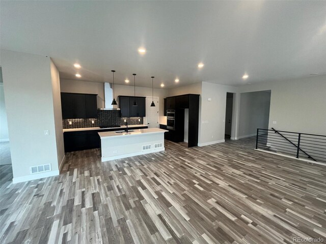 1613 Winter Glow Dr, Windsor, CO 80550 - kitchen with wall chimney exhaust hood, open floor plan, wood finished floors, dark cabinetry, and light countertops