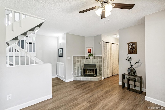 3612 Rosewalk Cir, Highlands Ranch, CO 80129 - unfurnished living room featuring ceiling fan, stairs, wood finished floors, a textured ceiling, and a tiled fireplace
