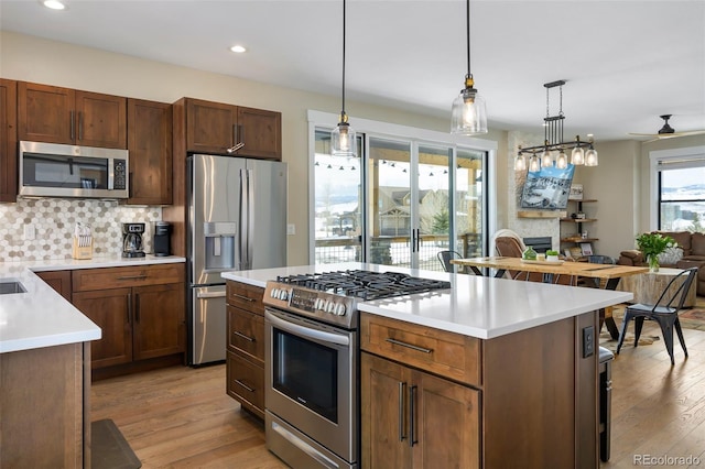 kitchen with stainless steel appliances, light wood-style floors, hanging light fixtures, light countertops, and tasteful backsplash