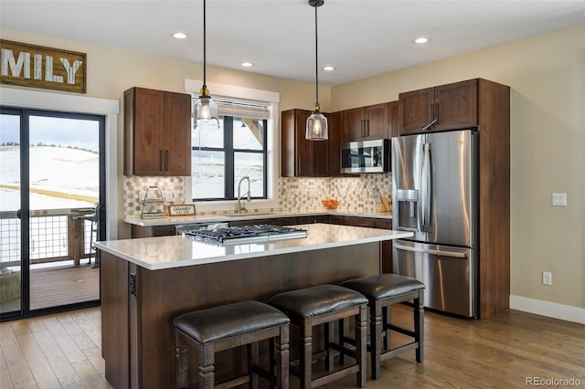 kitchen with decorative backsplash, stainless steel appliances, dark brown cabinets, light countertops, and a sink